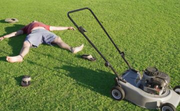 man laying down next to lawnmower after finishing mowing lawn