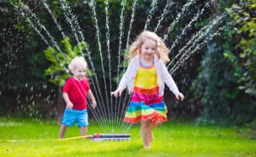 Kids playing in yard while sprinkler watering lawn