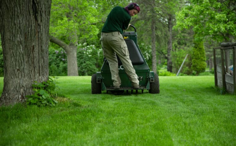 young woman providing lawn aeration service on riding aerator equipment to a green lawn