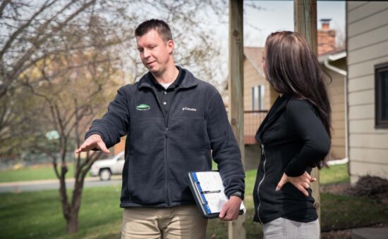 lawn care consultant speaking with homeowner while pointing to lawn